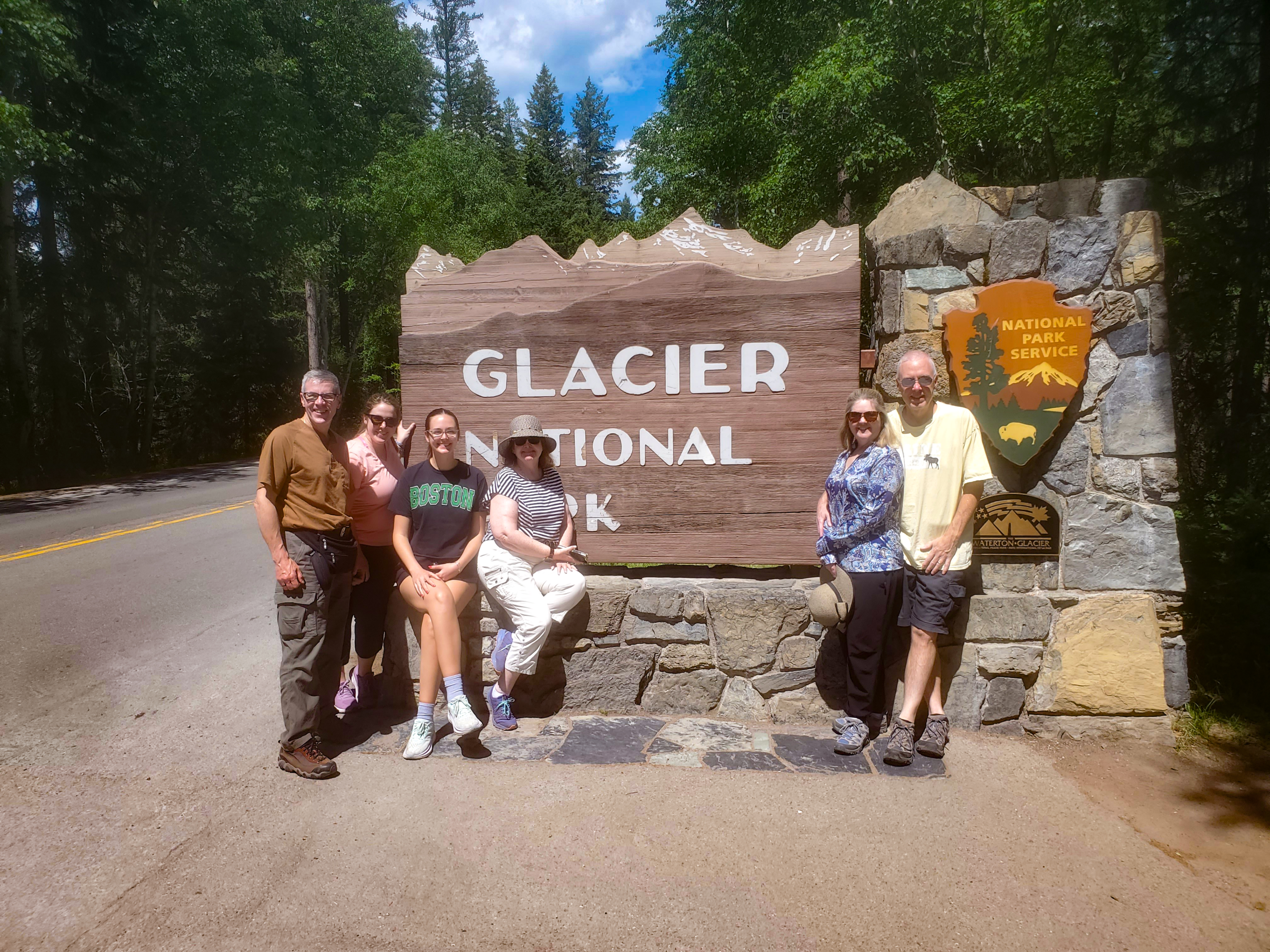 Family has a photo opportunity by the Glacier National Park Sign on a sunny day