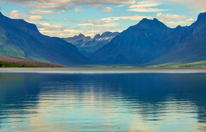 Scenic view of Lake McDonald in Glacier National Park with calm water reflecting dramatic clouds and towering mountain peaks in the distance.